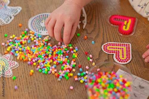 Child creating thermomosaic hearts with ironing beads fuse beads on wooden table