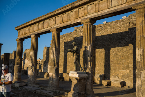 Konstfotografi Warm evening sunlight illuminates fluted stone columns and a bronze statue at the Temple of Apollo in Pompeii, Italy