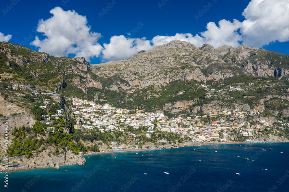 Obraz premium An expansive aerial perspective reveals the coastal village of Positano, Italy, nestled between steep limestone cliffs and the deep blue waters of the Amalfi Coast. The dramatic mountains rise above