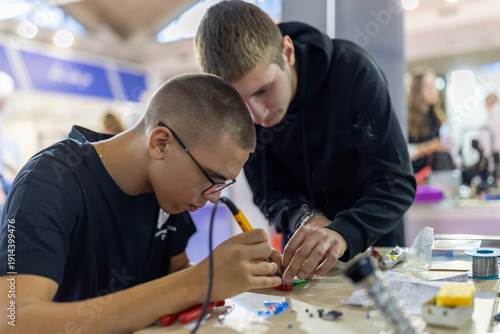 Young men learning electronics soldering skills in workshop