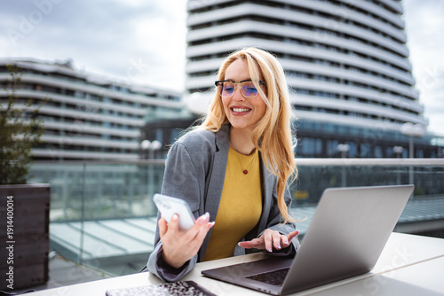 Wallpaper Mural Woman smiling while using phone and laptop on a city patio Torontodigital.ca