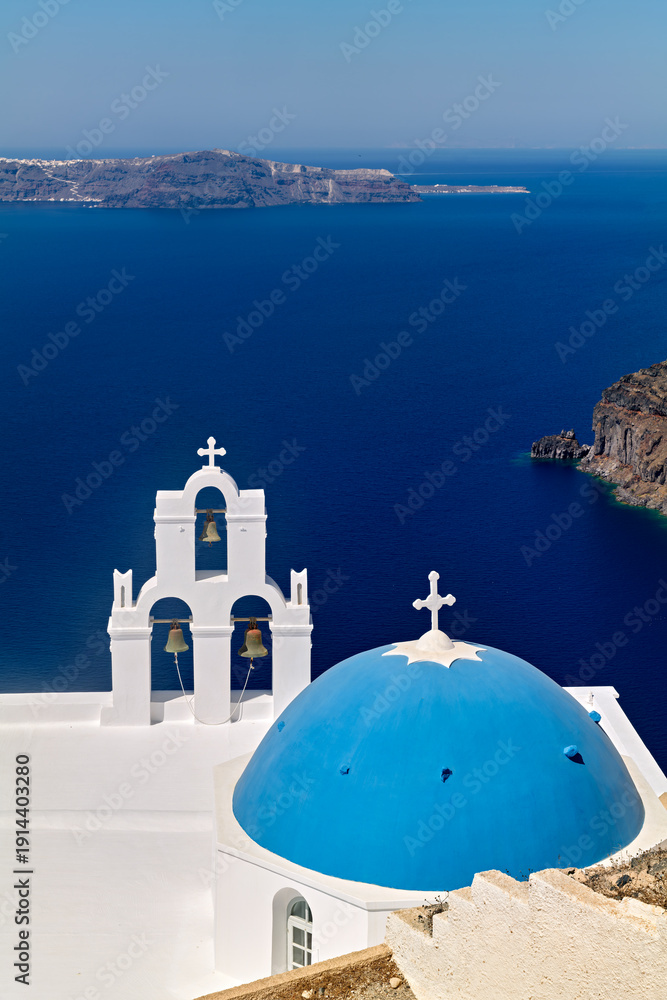 Fototapeta premium Blue-domed church and bell tower overlooking Santorini's caldera.