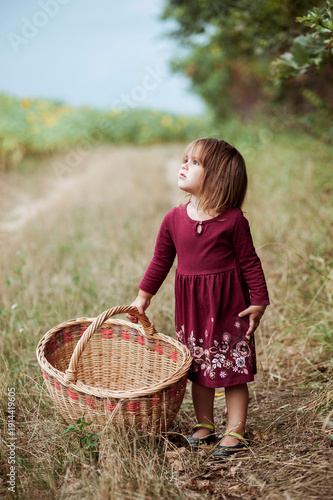 Little girl holding wicker basket on countryside path looking upward