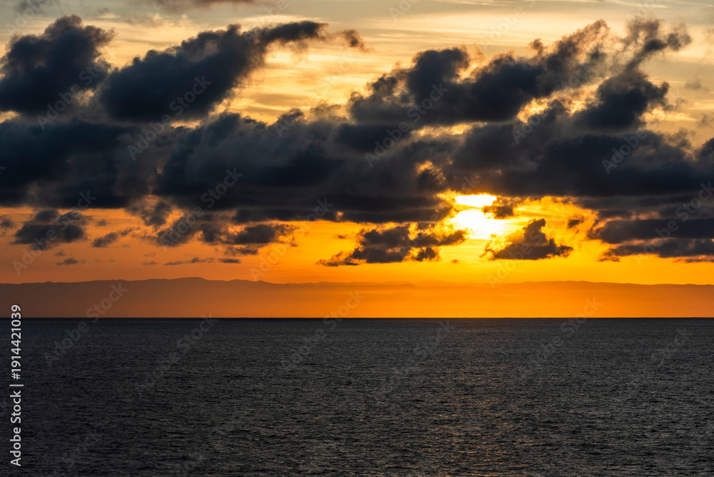 Fototapeta premium Distant mountain outlines along the Chilean coast illuminated by a vivid orange sunrise sky.
