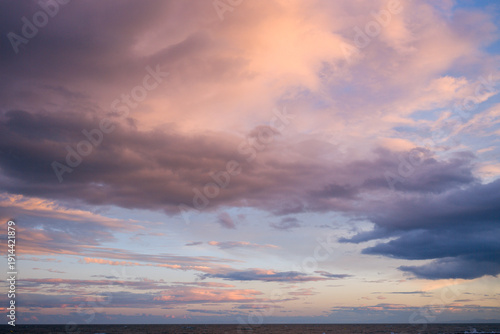 Expansive layers of pink, lavender, and blue clouds stretch across the sky above the calm sea near Agde, capturing the tranquil mood of a summer evening with soft, shifting light and subtle gradients.