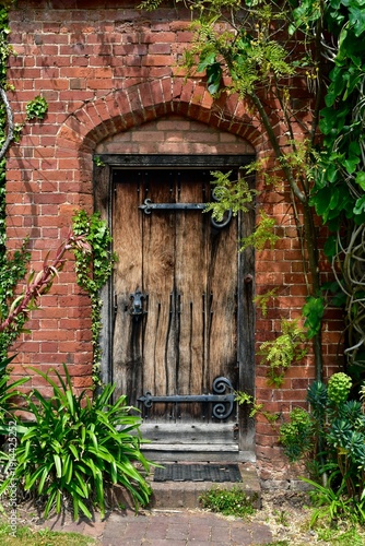 Exterior view of an old wooden door in a red brick wall into the garden, England, UK