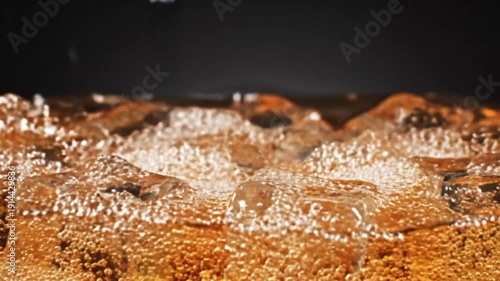 Dramatic high-speed macro shot captures the mesmerizing crown splash as a single drop impacts amber liquid swirling over solid ice cubes in a close-up beverage concept.