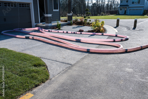 Long pink hose, patched with silver duct tape, looped in driveway of new home build, ready to blow in insulation, residential housing development
