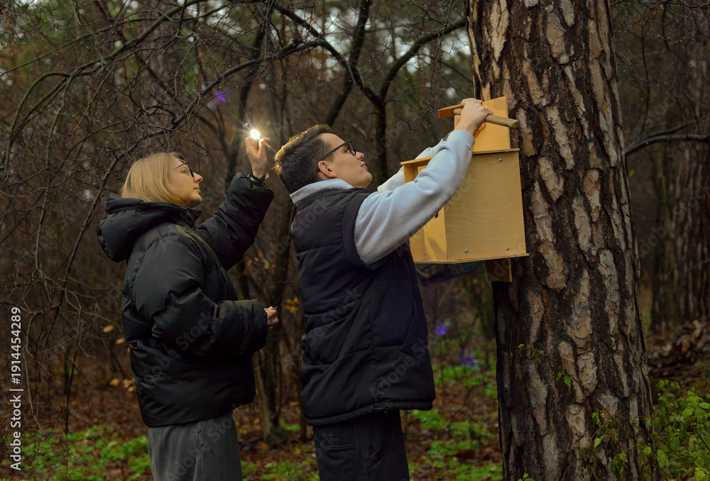 Naklejka premium A young man and woman hang a birdhouse on a tree