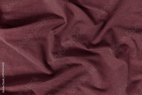 Detailed texture of a corduroy fabric background. Top view of a rich burgundy, maroon, wine tone textile material softly draped to create an abstract background