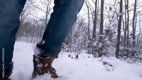 Close-up shot follows a man walking in trekking boots along a snowy trail. Slow motion emphasizes footprints, winter textures, and peaceful forest hiking in Nova Scotia, Canada.