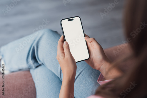Slika na platnu Close-up of a young woman relaxing at home while holding a smartphone with a bla