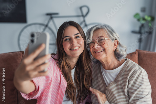 Φωτογραφία An excited adult daughter and her senior mother hold a phone to capture a selfie
