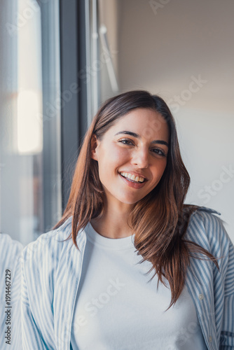 Valokuva A confident young woman smiles naturally at the camera near a window, captured i