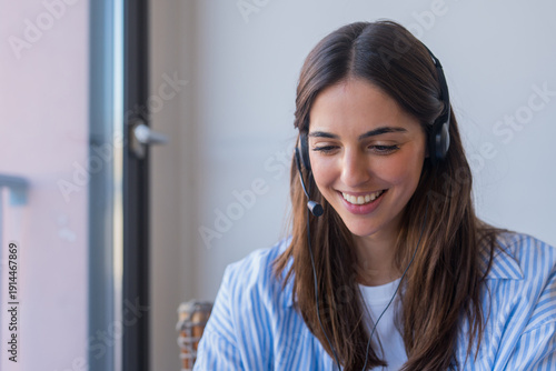 Tablou pe pânză A friendly young woman with a headset looks at the camera while assisting client