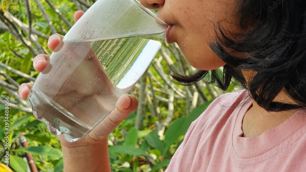 Fototapeta premium East Asian girl drink a glass of pure water with natural background. Healthy life style concept.