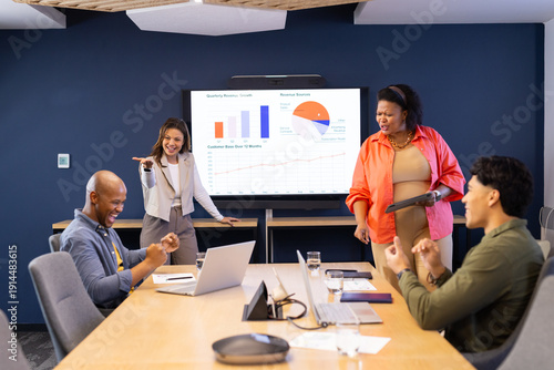 Diverse coworkers analyzing revenue growth charts on boardroom display with laptop and tablet