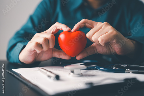 Hands holding red heart above medical documents and stethoscope symbolizing preventive healthcare heart awareness insurance and wellness protection concept