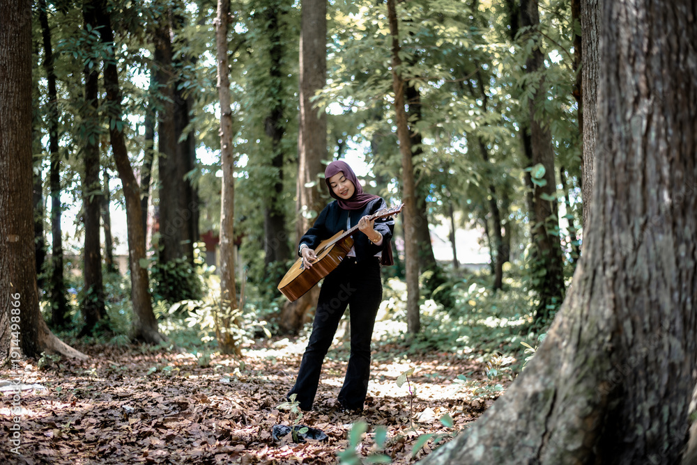 Fototapeta premium Woman in headscarf playing stringed instrument in sunlit forest
