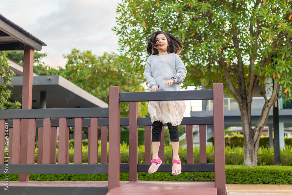 Obraz premium Excited Asian girl laughing happily on the high platform of a wooden playground structure