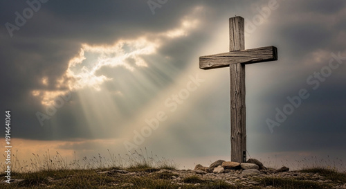 A weathered wooden cross stands on a rocky hilltop under a dramatic cloudy sky with sun rays breaking through