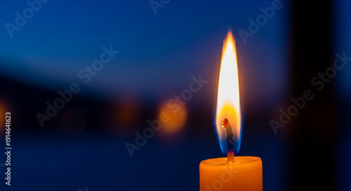 A single lit candle with a warm flame against a dark blurred background at dusk or dawn