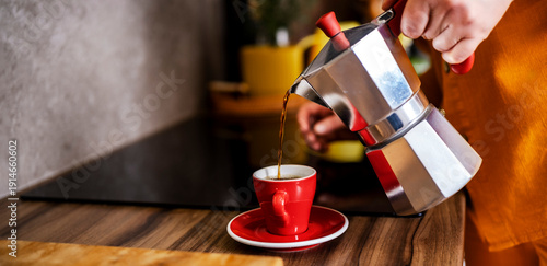 Tablou pe pânză Woman pouring fresh espresso from moka pot into red cup