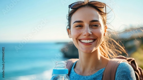 Smiling woman outdoors by the sea holding a water bottle on a sunny day