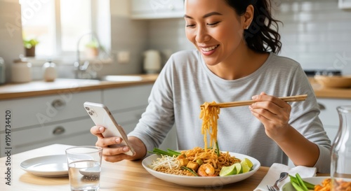 Modern dining experience: Smiling woman with smartphone enjoying delicious noodle dish at home