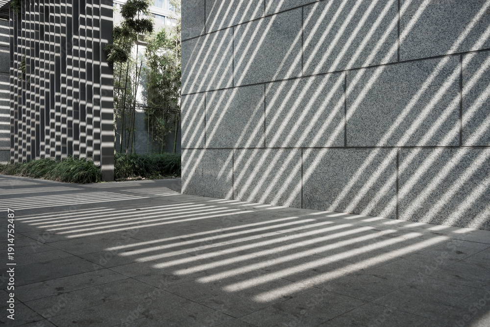 Fototapeta premium Modern architectural facade casting striped light and shadow patterns on stone pavement and wall surface