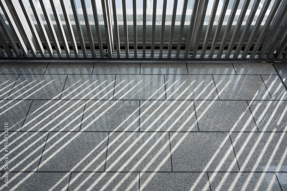 Fototapeta premium Metal railing casts diagonal shadows on gray tiled floor