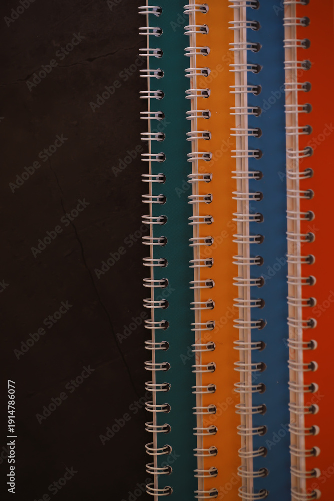Fototapeta premium Colorful Spiral Notebooks Against Dark Background - Vibrant Stationery Organization Concept