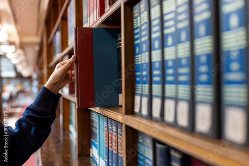 Hand selecting book from wooden library shelf. Legal research concept, attorney reference material, system study, academic knowledge and professional legislation archive.