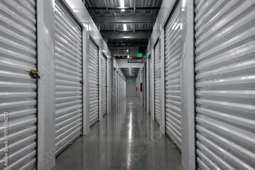 Long corridor inside a modern self storage facility. Empty storage hallway with metal roll up doors. Clean and secure indoor storage units for rent. Symmetrical storage corridor with industrial.