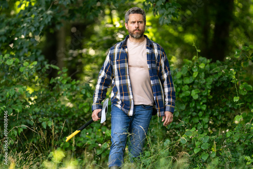 Handsome man or lumberjack in checkered shirt hold axe. Lumberjack or woodman. Masculinity concept. Man brutal strong attractive guy cutting wood with axe in forest. Lumberjack with big axe in forest.