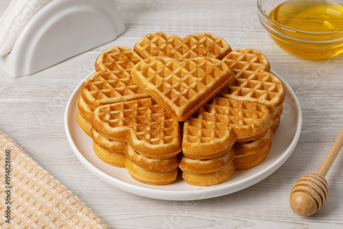 Waffles made in a heart shape served on a plate with honey and syrup nearby
