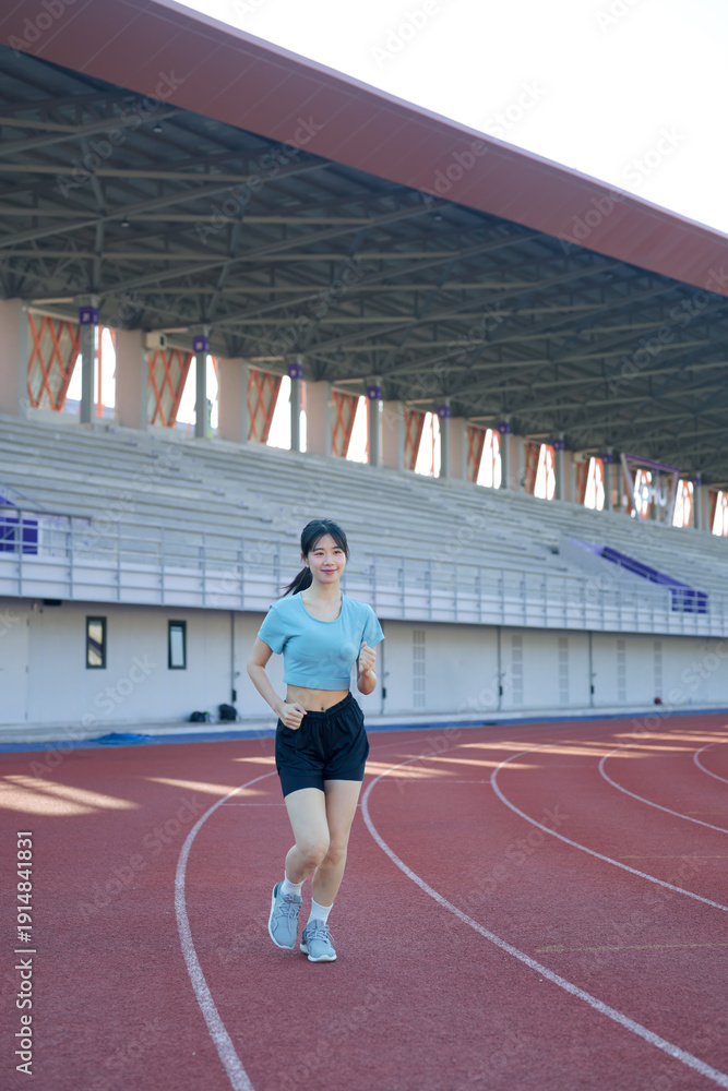 Obraz premium Young Asian woman jogging on outdoor running track at stadium, morning exercise