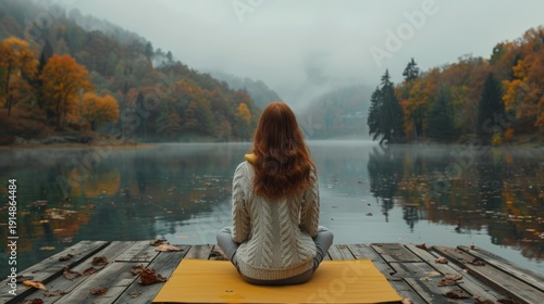 Red-haired person meditates on dock by a serene, misty autumn lake with vibrant trees