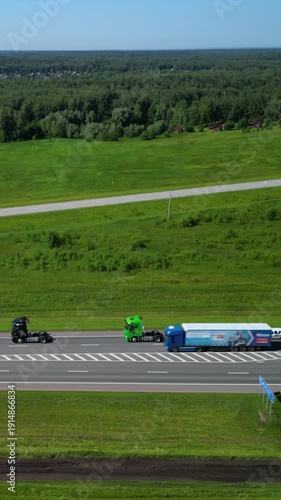 Aerial Highway Trucks Overtaking In Countryside, Two Tractor Units Passing On Multi Lane Road Beside Green Fields Under Clear Sky, Fast Motion, Visible Traffic Merging And Distant Forest Horizon