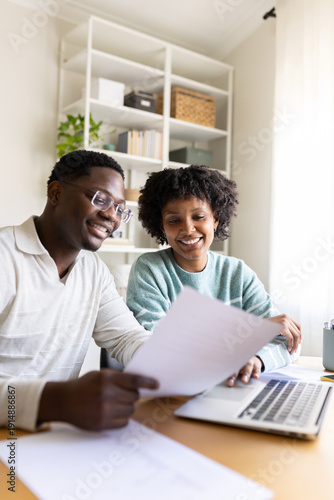 Canvas Print Smiling black couple reviewing documents and using laptop at home