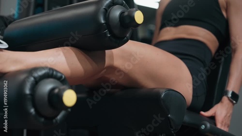 Athletic woman training legs on a leg extension machine in a modern gym. Focused strength workout targeting quadriceps. Concept of fitness routine, muscle toning, healthy lifestyle, strength training