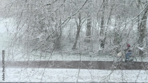 Blurry and fast cyclists riding under a heavy snow accros the leaveless trees