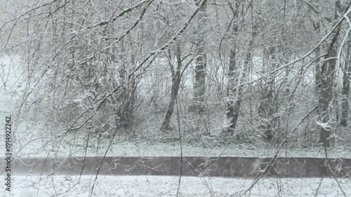 Blurry and fast cyclists riding under a heavy snow accros the leaveless trees