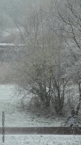 Blurry and fast cyclists riding under a heavy snow accros the leaveless trees