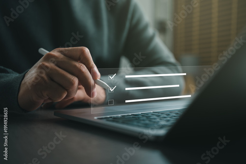 Photos Business professional completing an online checklist on a virtual interface using a stylus and laptop