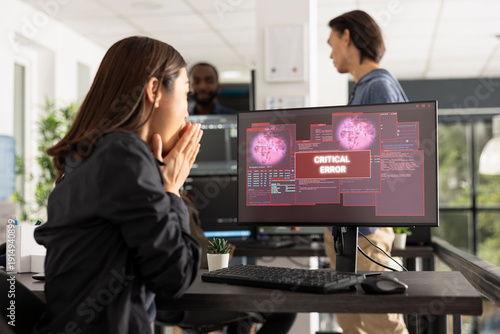 Portrait of female programmer reacting to alarming error alert on desktop monitor. Woman covers mouth in panic, representing software bugs, cyberattack threats and digital security crisis.