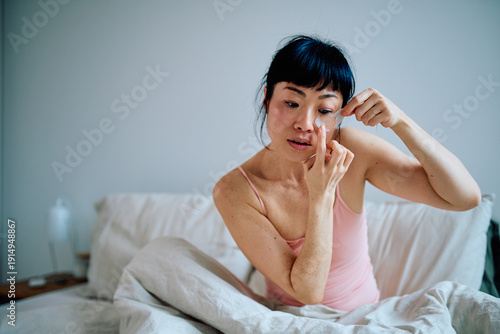 Schilderij op canvas Young Asian woman applying refreshing under eye patches while relaxing in bed, p