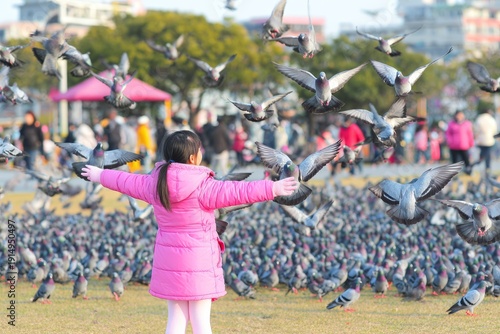 Child in Pink Jacket Surrounded by Flying Pigeons in Park Setting