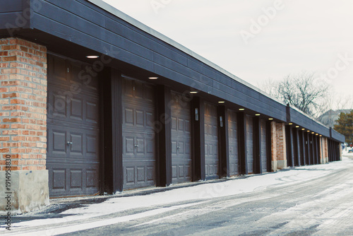 Storage units are lined up in a row showing gray doors with some snow on the ground in a location during winter