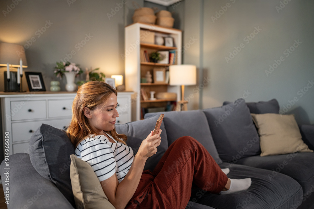 Obraz premium Woman relaxing at home checking smartphone on couch